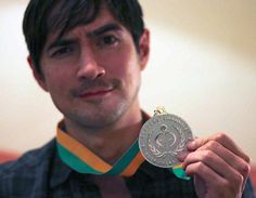 a man holding up a silver medal in his right hand and looking at the camera