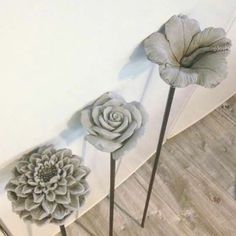 three metal flowers are placed next to each other on the floor in front of a white wall