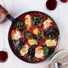 a pan filled with eggs and spinach on top of a table next to glasses of wine