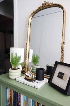 a green table topped with a mirror next to a shelf filled with books and plants