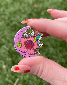 a woman's hand holding a pink and purple pin with flowers on the front