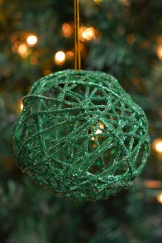 a green ball ornament hanging from a christmas tree with lights in the background