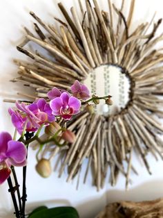 a vase filled with purple flowers sitting next to a wall mounted sunburst mirror