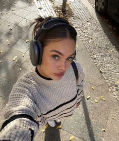 a young woman wearing headphones on the sidewalk with her hand up to her face