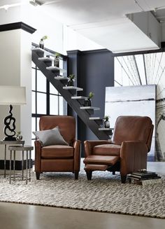 two brown leather chairs sitting in front of a stair case