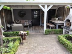 a covered patio with seating and tables in the back yard, surrounded by greenery