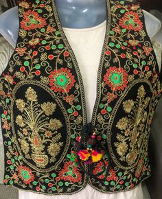 This is a beautiful Indian colorful vest. It is primarily full of green, gold and red embroidery on a black base in lovely floral designs with decorative leaves throughout the front. This is a lovely piece to wear on top of traditional Indian clothing or a regular T-shirt to add a dash of color to your outfit. The back of the vest is plain black except a small strip of embroidery work at the base of the vest.  This is a handmade piece, so there may be slight imperfections throughout this piece. Noir Uni, Colorful Vest, Suit Salwar, Quinceanera Ideas, Decorative Leaves, Waist Coat, Brown Vest, Afghan Dresses, Red Embroidery