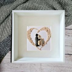 two rocks in the shape of a heart are placed inside a white shadow box on a wooden surface