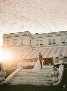 a bride and groom standing on steps in front of a large building with striped awnings