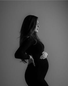 a pregnant woman poses for a black and white photo with her hands on her hips