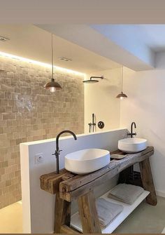 two white sinks sitting on top of a wooden table next to a wall mounted faucet