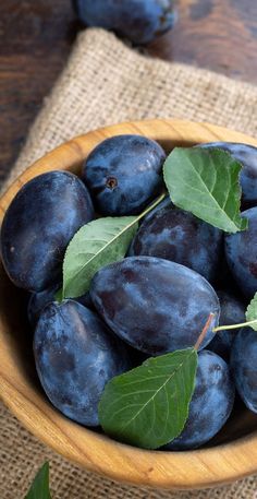 a wooden bowl filled with blue plums and green leaves on top of a table