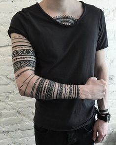 a man with tattoos on his arm standing in front of a white brick wall