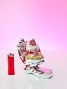 an ice cream sundae in a silver dish with a red lighter next to it