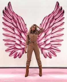 a woman standing in front of a giant pink angel wings