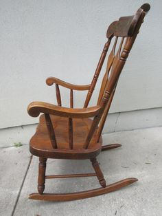 a wooden rocking chair sitting on top of a cement floor next to a white wall