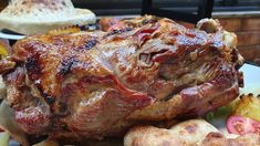 a large piece of meat sitting on top of a white plate next to potatoes and tomatoes