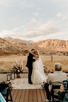 a bride and groom kissing on the deck at their outdoor wedding ceremony in the mountains