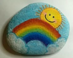 a painted rock with a smiling sun and rainbow on it's face in the clouds