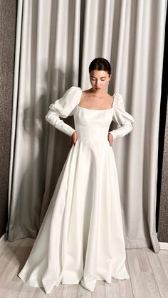 a woman standing in front of a curtain wearing a white dress with puffy sleeves