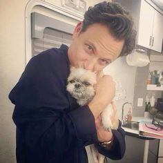 a man is holding a small dog in his arms and smiling at the camera while standing in front of an oven