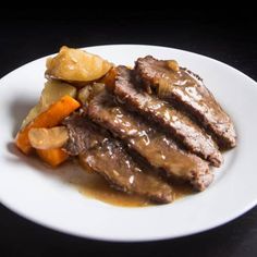 a white plate topped with meat and veggies on top of a black table