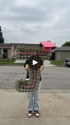 a person standing in the middle of a street wearing a paper mache hat and holding a pink box