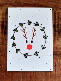 a christmas card with a reindeer's head and green leaves on the front, sitting on a wooden table