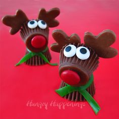 three chocolate reindeers with googly eyes and green leaves on their heads, sitting on a red surface