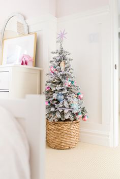 a small christmas tree in a wicker basket on the floor next to a bed