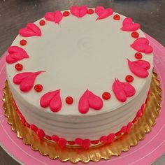 a white cake with pink icing and red hearts on the top is sitting on a gold plate