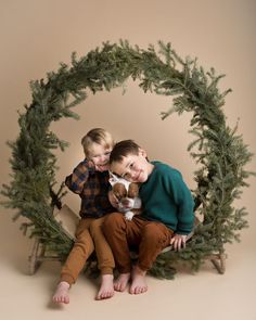 two young boys sitting in front of a christmas wreath with a dog on his lap