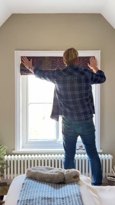 a man standing on top of a bed in front of a window next to a radiator