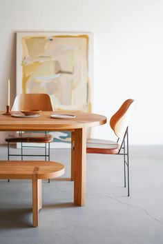 a wooden table with two chairs and a painting on the wall in the back ground