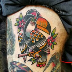 a colorful bird tattoo on the side of a man's thigh