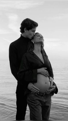 a man and woman standing next to each other near the ocean with their belly wrapped around them