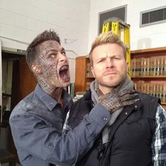 two men with face paint on their faces in a room full of bookshelves