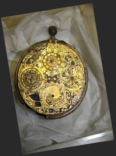 an antique pocket watch with gold and black designs on the front, in a box