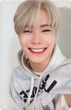 a person with blonde hair wearing a white hoodie and smiling at the camera while posing for a photo