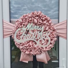 a woman standing in front of a door holding a pink wreath with merry christmas written on it