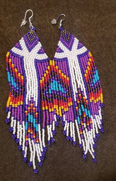 Beautiful hand beaded tassel earrings in white,  purple,  blue,  gold,  red,  orange and yellow.  These are 5.5 inches long and 1.5 inches wide in a stunning bohemian design.  Shades of blue,  gold and purple form a diamond on top with white leading to the multicolored tassels.   These earrings are the perfect accessory for a western style outfit,  with jeans or even a dress. Outfit With Jeans, Gold And Purple, Western Style Outfits, Beaded Tassel Earrings, Boho Design, Bohemian Design, Wedding Jewelry Earrings, Orange And Yellow, Beaded Tassels