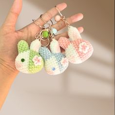 a hand holding three small knitted keychains in the shape of animals, one with a green bead on it's ear