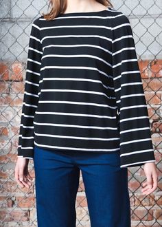 Inspired by a recent trip to France, the Breton Top or marinière, always takes us back to walking down Av. Kléber. Also influenced by its nautical beginnings, this striped top is a common KF go-to. Boat neck, stretch modal body, bell sleeve. Loose through body and hem hits at waist. 62% Rayon, 19% Cotton, 13% Modal, 6% Spandex. Slips on. Made in USA. Model is wearing XS. Need help with sizing? Size Guide Crew Neck Top With Striped Collar For Work, Crew Neck Top With Contrast Stripes For Work, Black Striped Cuffs Tops For Work, Black Tops With Striped Cuffs For Work, Black Workwear Tops With Striped Cuffs, Sailor Style Striped Long Sleeve Top, Striped Sailor Long Sleeve Top, Sailor Striped Long Sleeve Top, Long Sleeve Horizontal Stripe Workwear Top