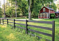 a red house sitting on top of a lush green field next to a wooden fence