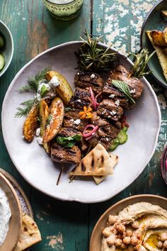 a white plate topped with meat and veggies next to pita breads