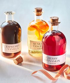 three bottles of various types of liquor on a table with a ribbon around them and two empty bottles next to each other