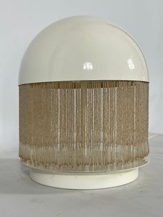 a white table lamp with gold fringes on the top and bottom, against a white background