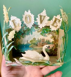 a person holding up a card with a swan on it and the word love spelled out