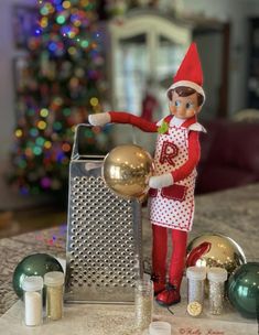 an elf is holding a golden ball in front of some christmas decorations on the table