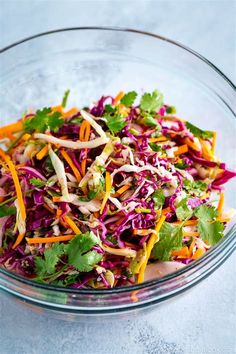 a salad in a glass bowl with carrots, cabbage and cilantro